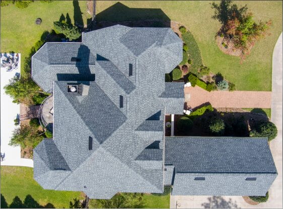 Aerial view of large residential home with gray shingle roof and landscaped yard