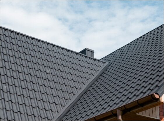 Modern gray tile roof with chimney against cloudy sky, residential roofing