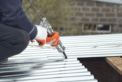 Worker applying sealant on metal roofing sheet with caulking gun