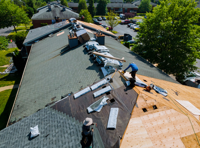 Workers repairing roof of large building using roofing materials and tools.