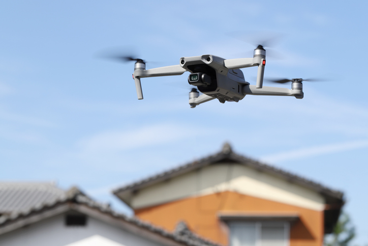 Drone hovering over rooftops under blue sky.