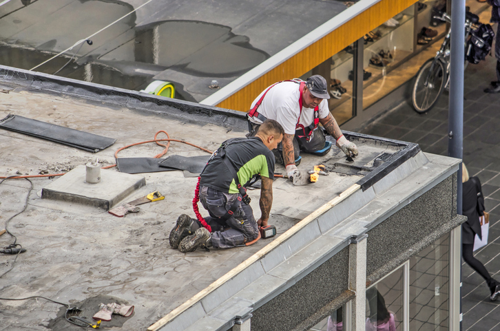 Two workers repairing a flat roof on a commercial building.