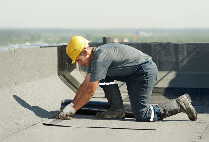 Construction worker installing roofing material on a flat roof.