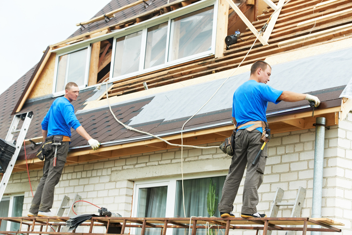 Two workers installing new roofing on a residential house.