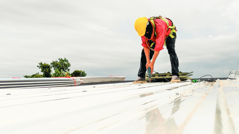 Construction worker installing metal roofing sheets outdoors.