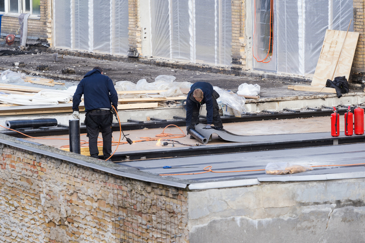 Workers installing roofing material on a flat building roof