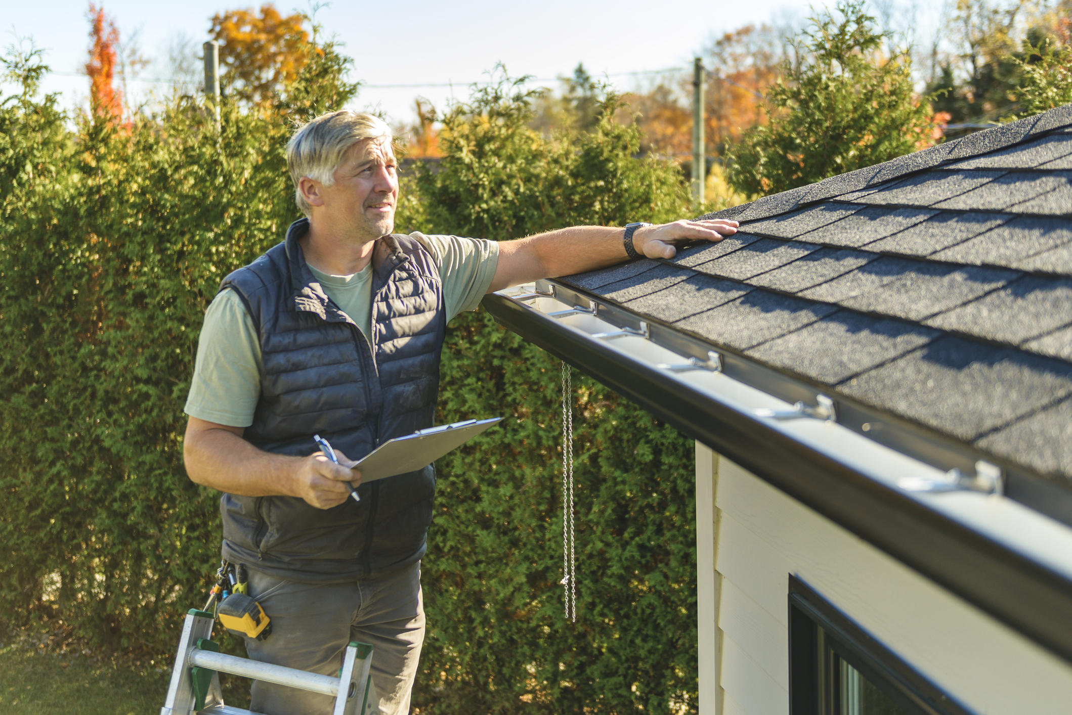 Inspector assessing a home's roof with clipboard and ladder