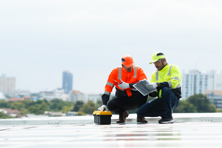 Two workers on a rooftop inspecting solar panels with safety gear.