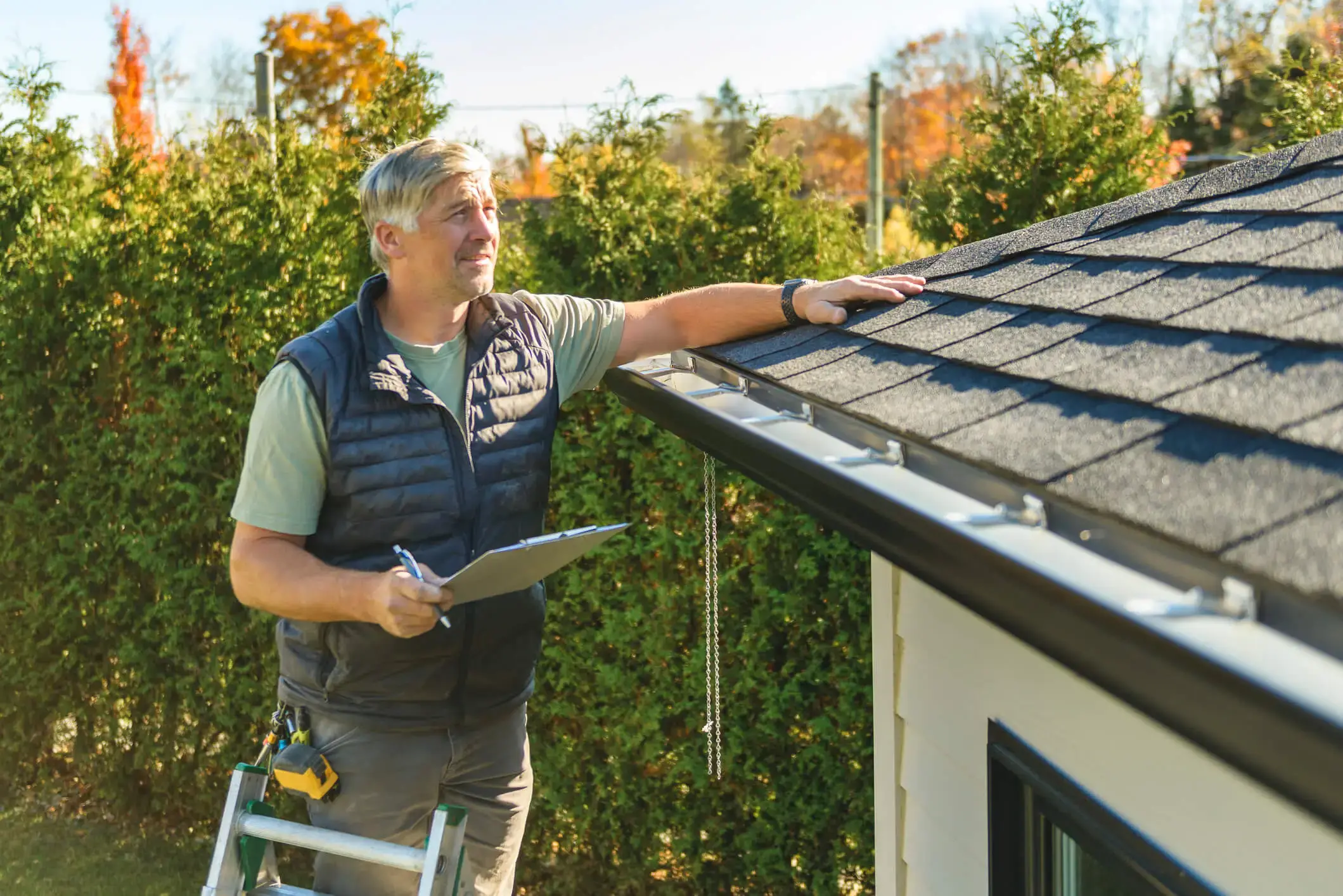 Man inspecting house roof shingles with clipboard in hand